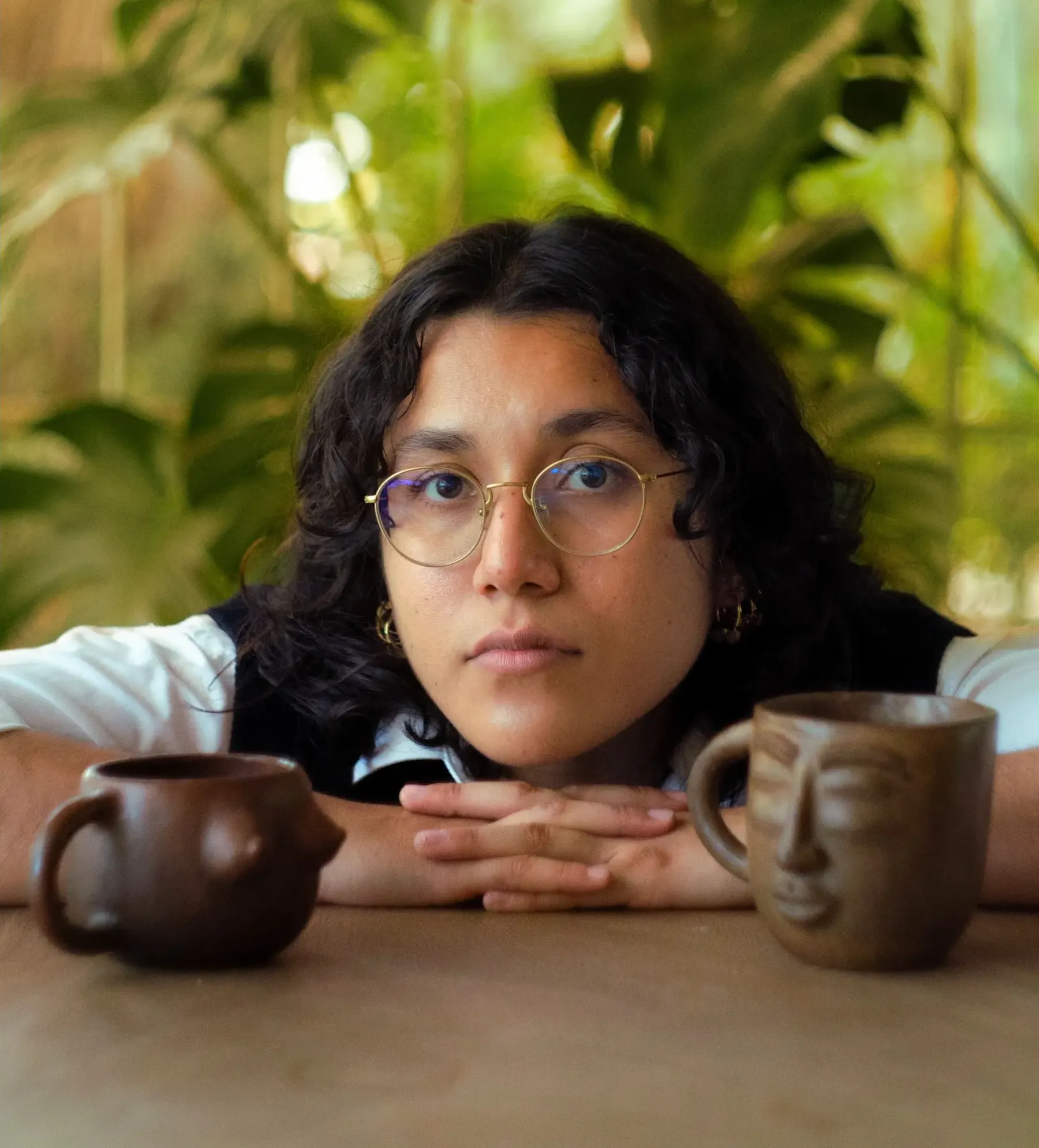 Retrato de Nelú apoyando los brazos sobre una mesa, junto a dos tazas de barro con rostros tallados.